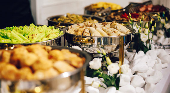 A crisp, white table with an assortment of a catered food spread in serving dishes.
